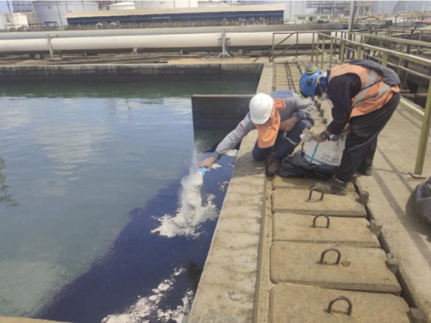 Response crews applying PRISTINE SEA clay powder from a dock, with white solidified oil cakes forming on the water