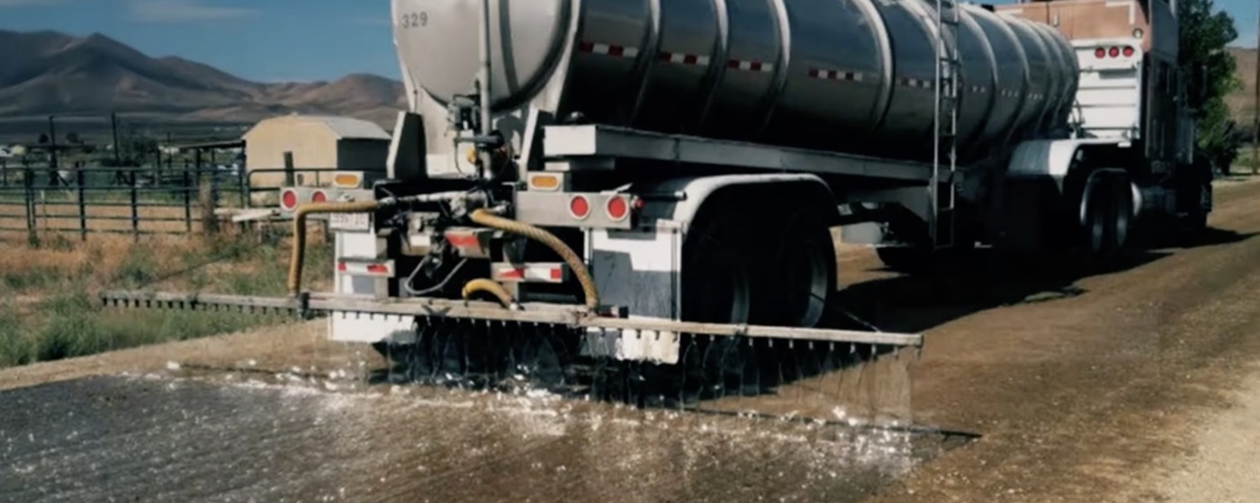 Spray-bar tanker truck applying diluted TRANS SEAL I dust suppressant on an unpaved road