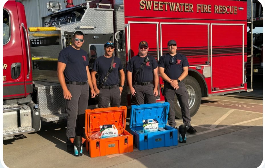 Four Sweetwater Fire Rescue firefighters standing behind an open orange ENVIRO-Z kit case and an open blue ENVIRO-G kit case in front of a fire engine